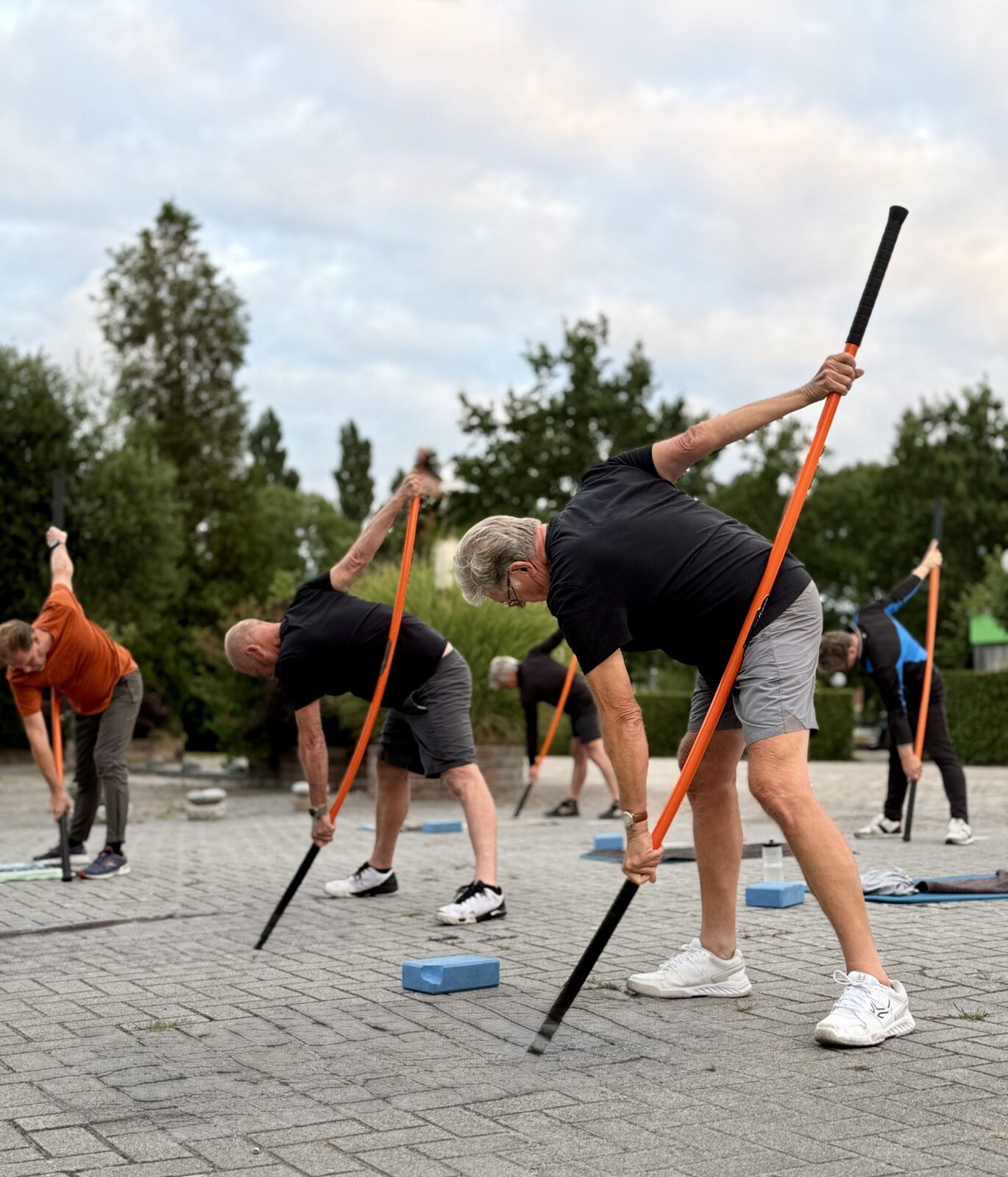 Mannen rekken zich buiten met oefenstokken tijdens functioneel rekken bij Keep Fit Joure